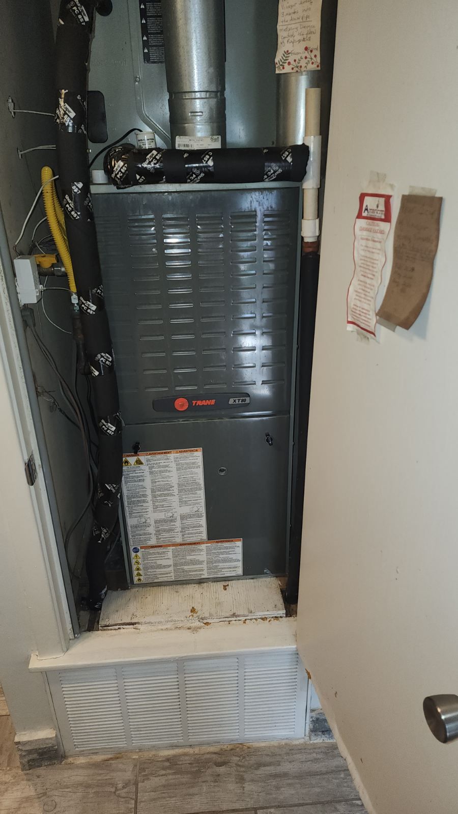 A furnace is sitting in a corner of a room next to a door.