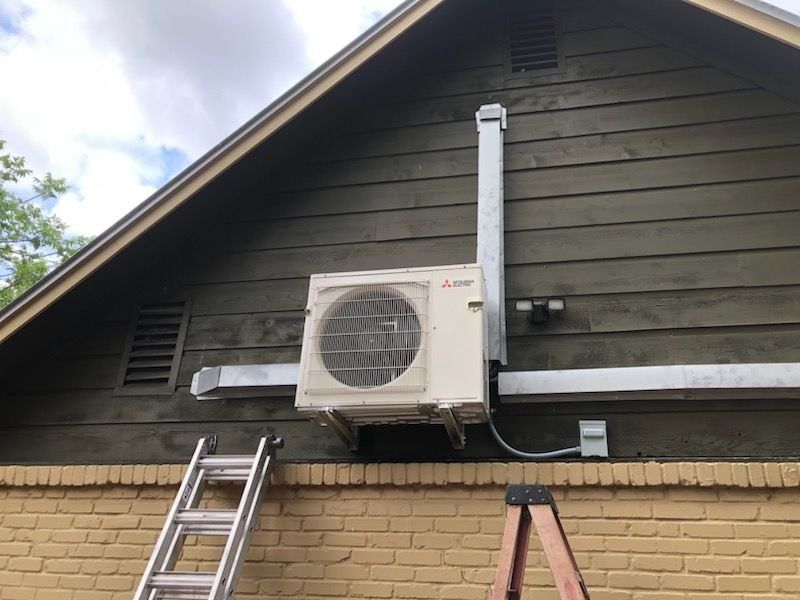 A ladder is sitting on the side of a building next to an air conditioner.