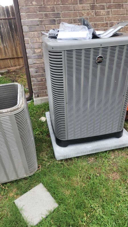 A large air conditioner is sitting in the grass next to a brick building.