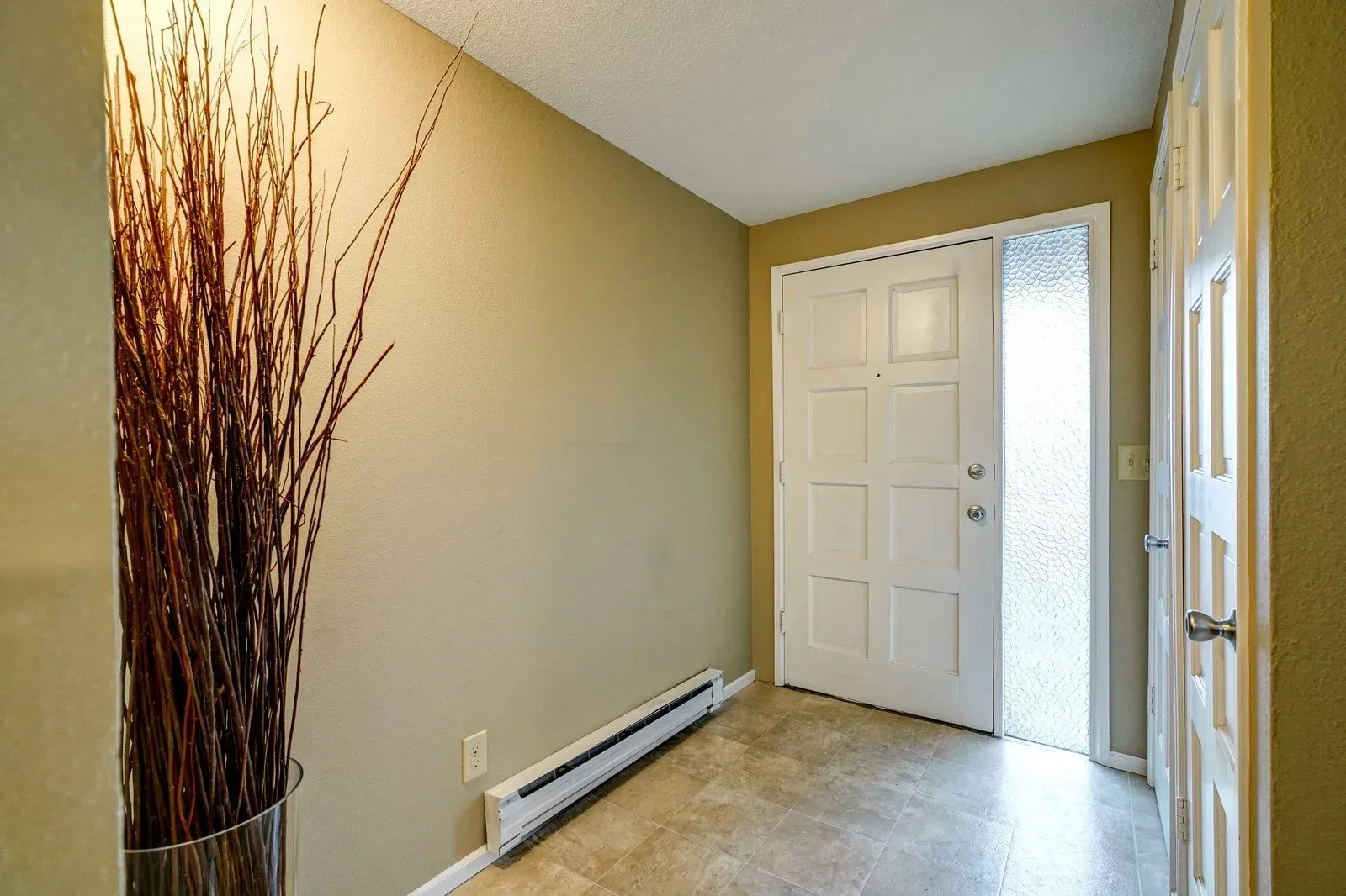 Hallway with beige walls, white door, and tall brown decorative reeds.