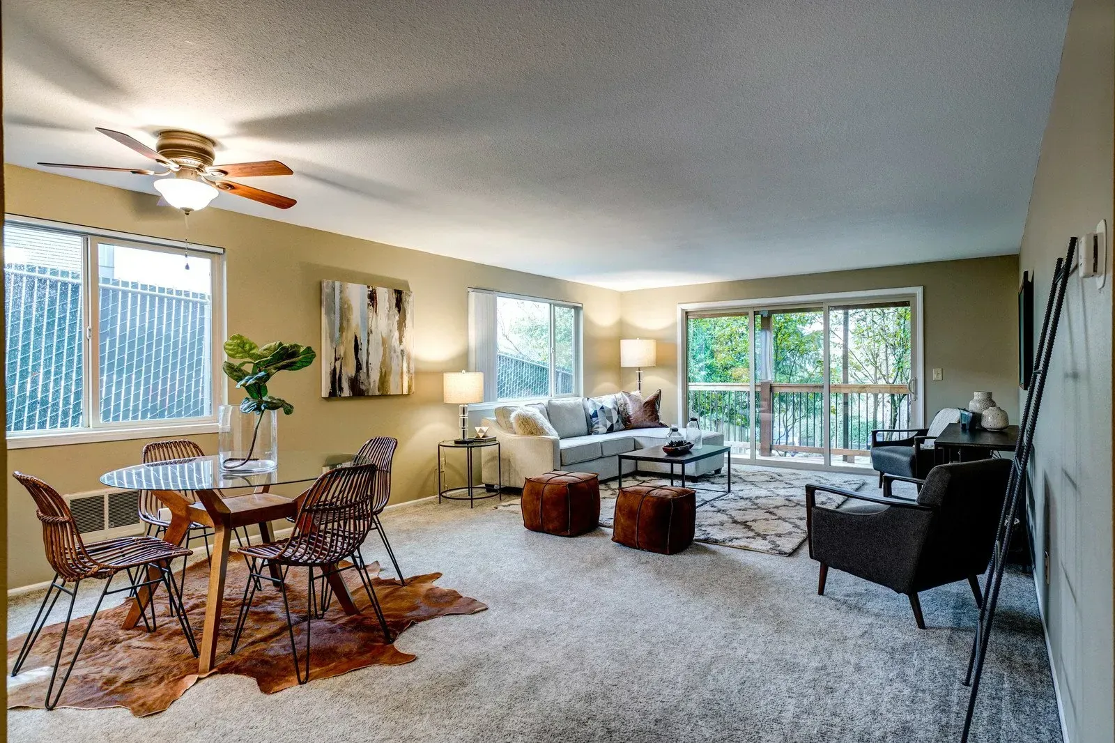 Living room with dining area, gray carpet, sofa, sliding door to balcony, neutral tones.