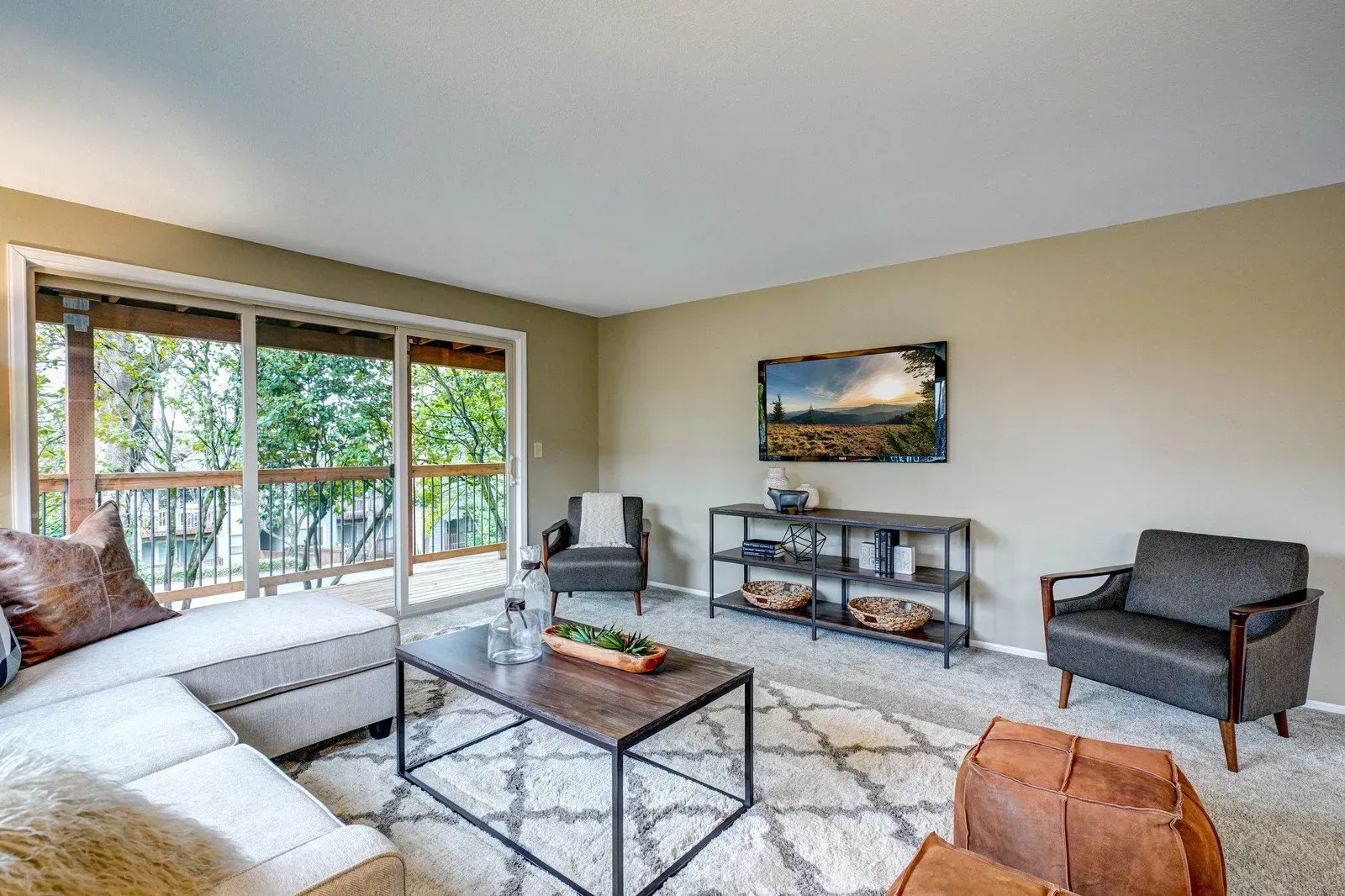 Living room with sectional, sliding door to balcony, TV, two armchairs, and coffee table.