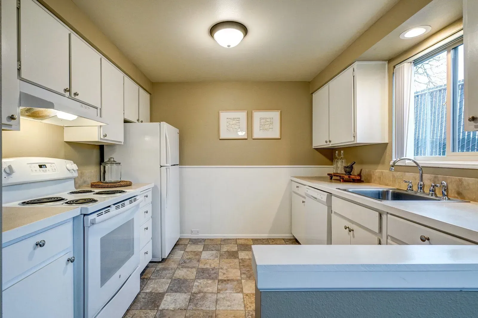 White kitchen with appliances and cabinets, beige walls, and window.
