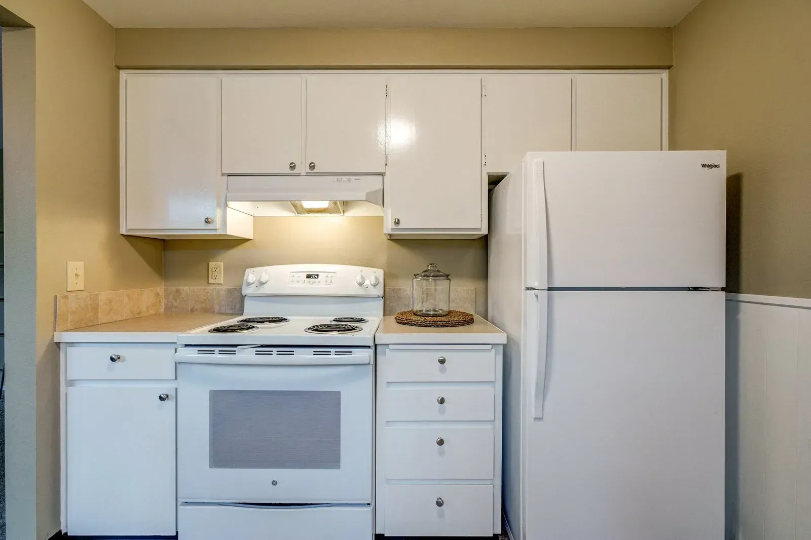 White kitchen with appliances, cabinets, and a stove. The refrigerator stands on the right.