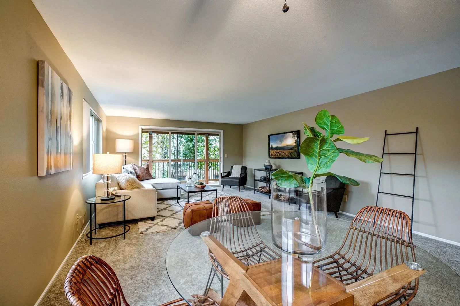 Living room with open dining area, glass table, wicker chairs, couch, rug, and greenery near sliding door.