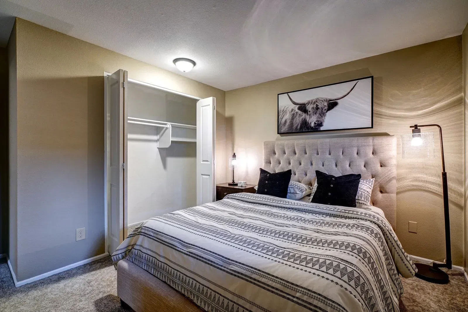 Bedroom with a bed, artwork of a bull, closet, lamp, and neutral color scheme.