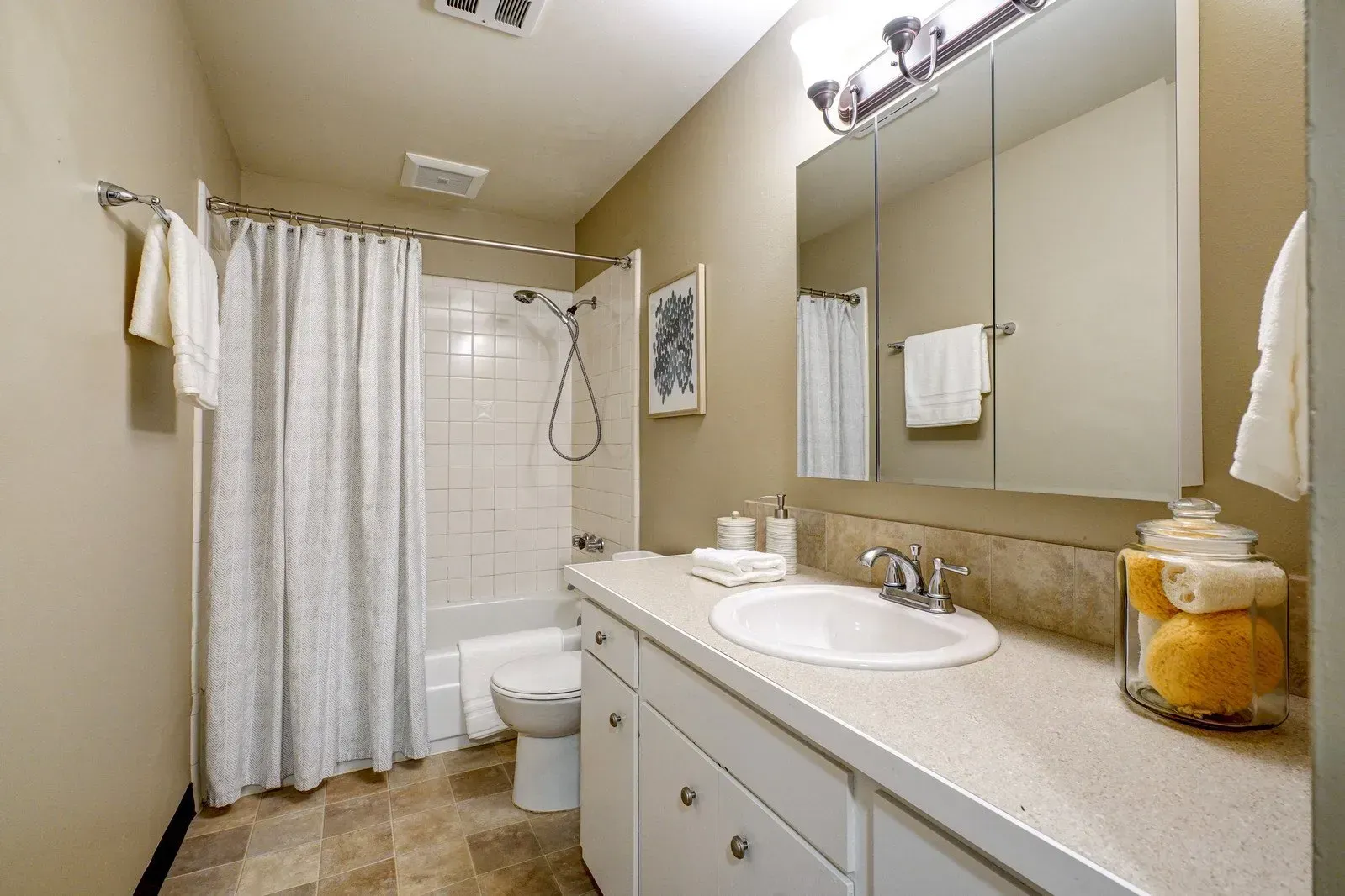 Bathroom with shower, vanity, toilet. Beige walls, white fixtures, and patterned shower curtain.