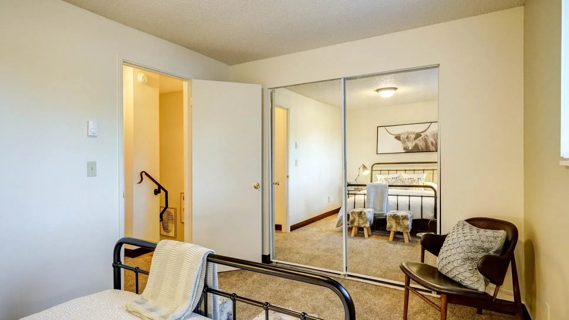 Bedroom with iron bed, open closet mirror reflecting bed, chair, and doorway.