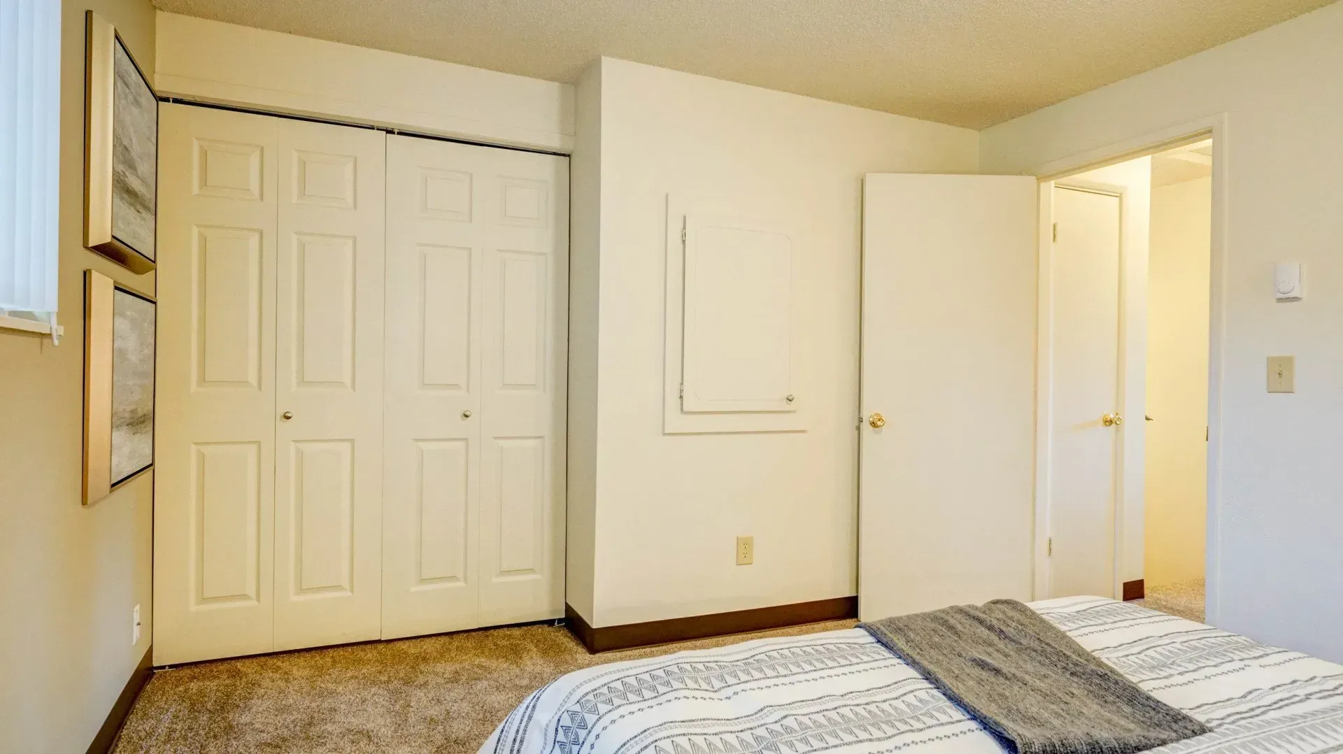 Bedroom with closed closet doors, open door to bathroom, bed with blanket, art on wall.
