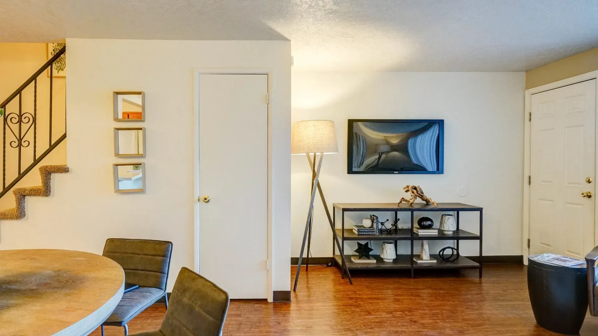 Living room with TV, shelves, floor lamp, stairs, and small wall art.