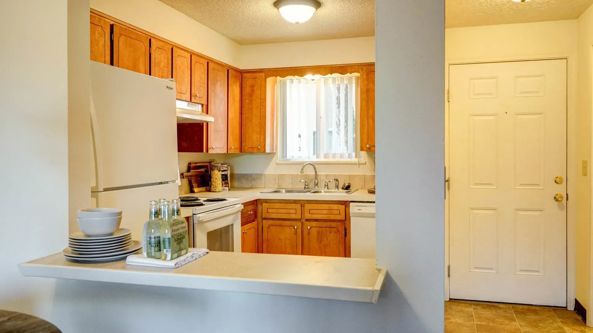 Kitchen with wood cabinets, white appliances, and a pass-through to a dining area with a white countertop.