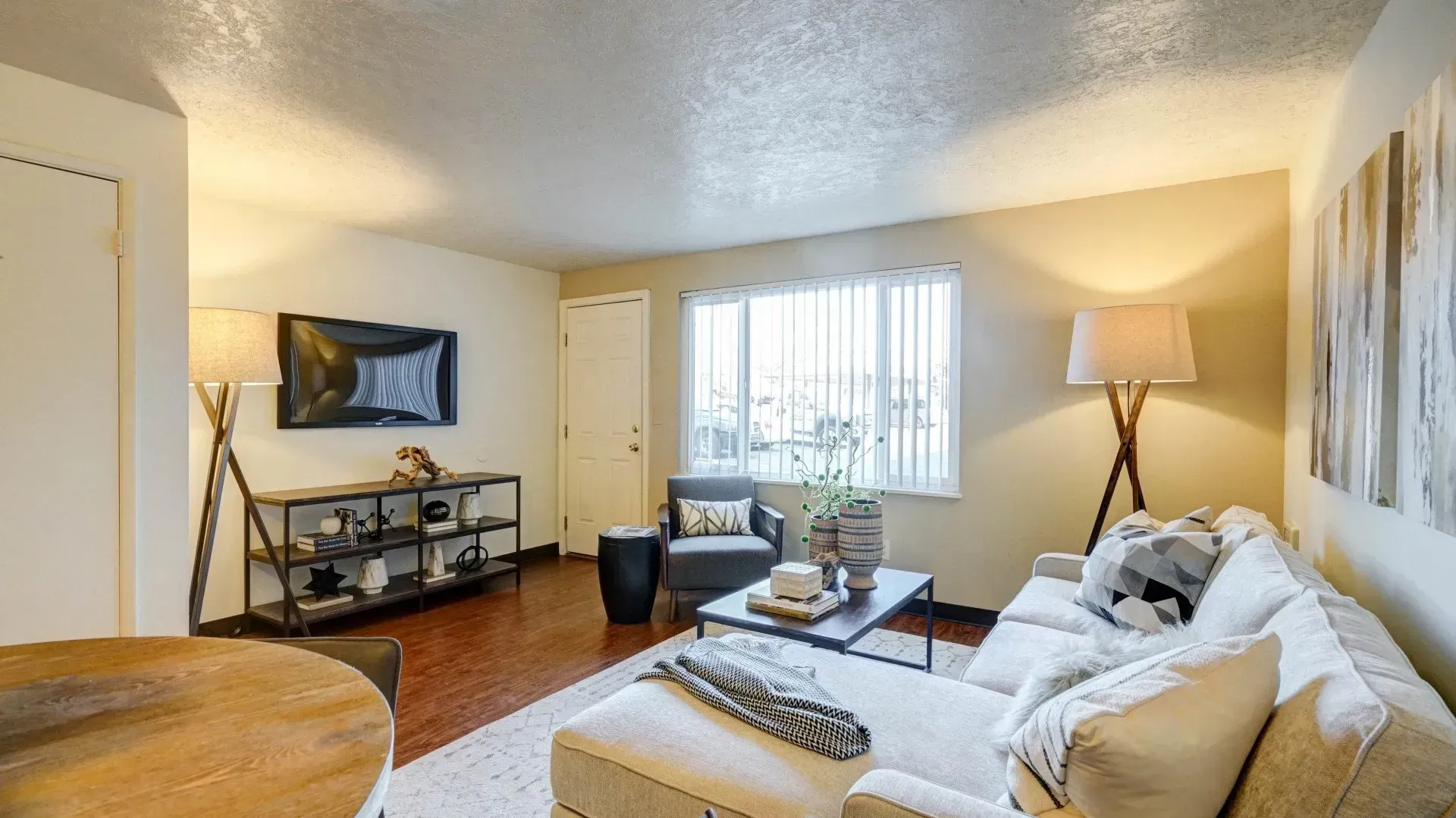 Cozy living room with cream-colored sectional sofa, dark wood floors, TV, and large window.