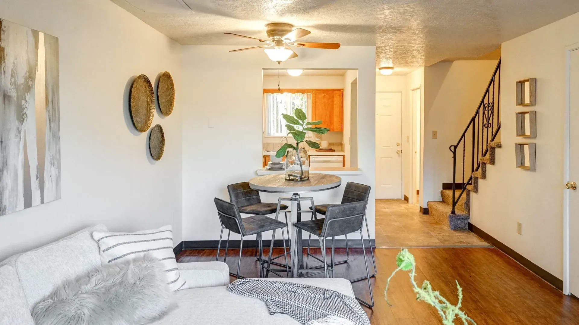 Living room with dining area, kitchen, and staircase. White walls, wooden floors, and modern furniture.