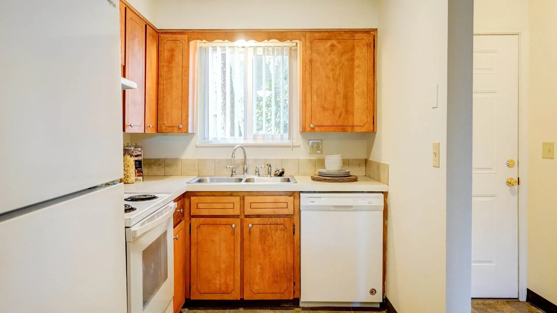 Kitchen with light brown cabinets, white appliances, and a window with blinds.