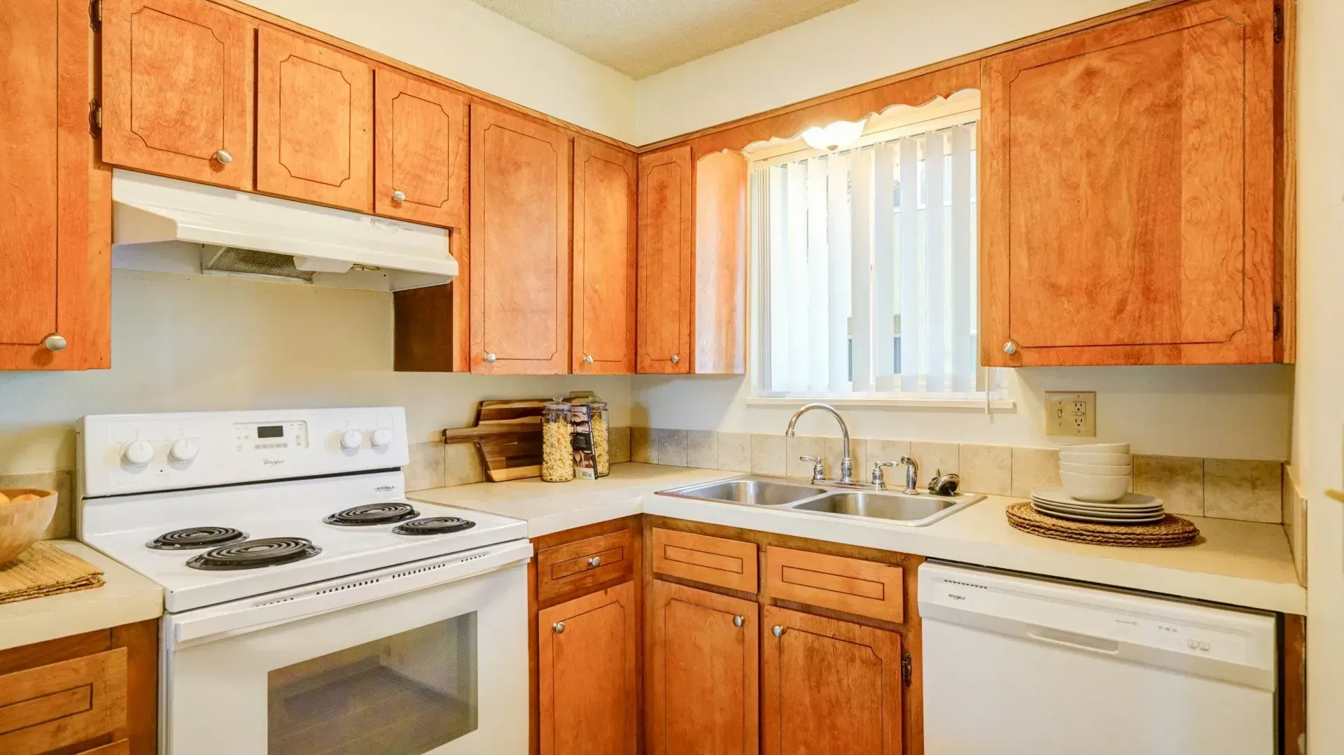 Kitchen with wooden cabinets, white appliances, and a window with a sheer curtain.