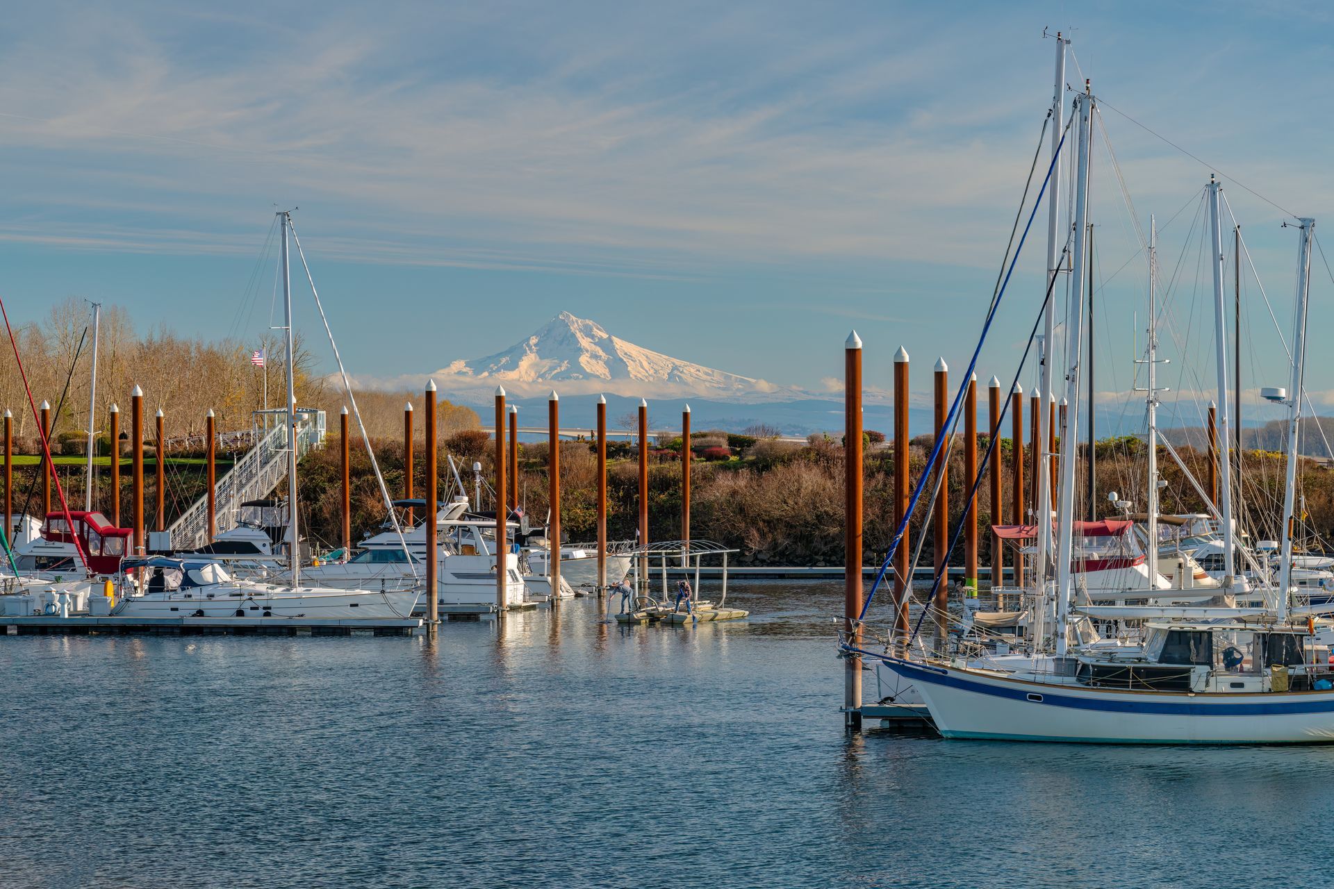 Sailboats docked in a marina, with snow-capped mountain in the background under a blue sky.