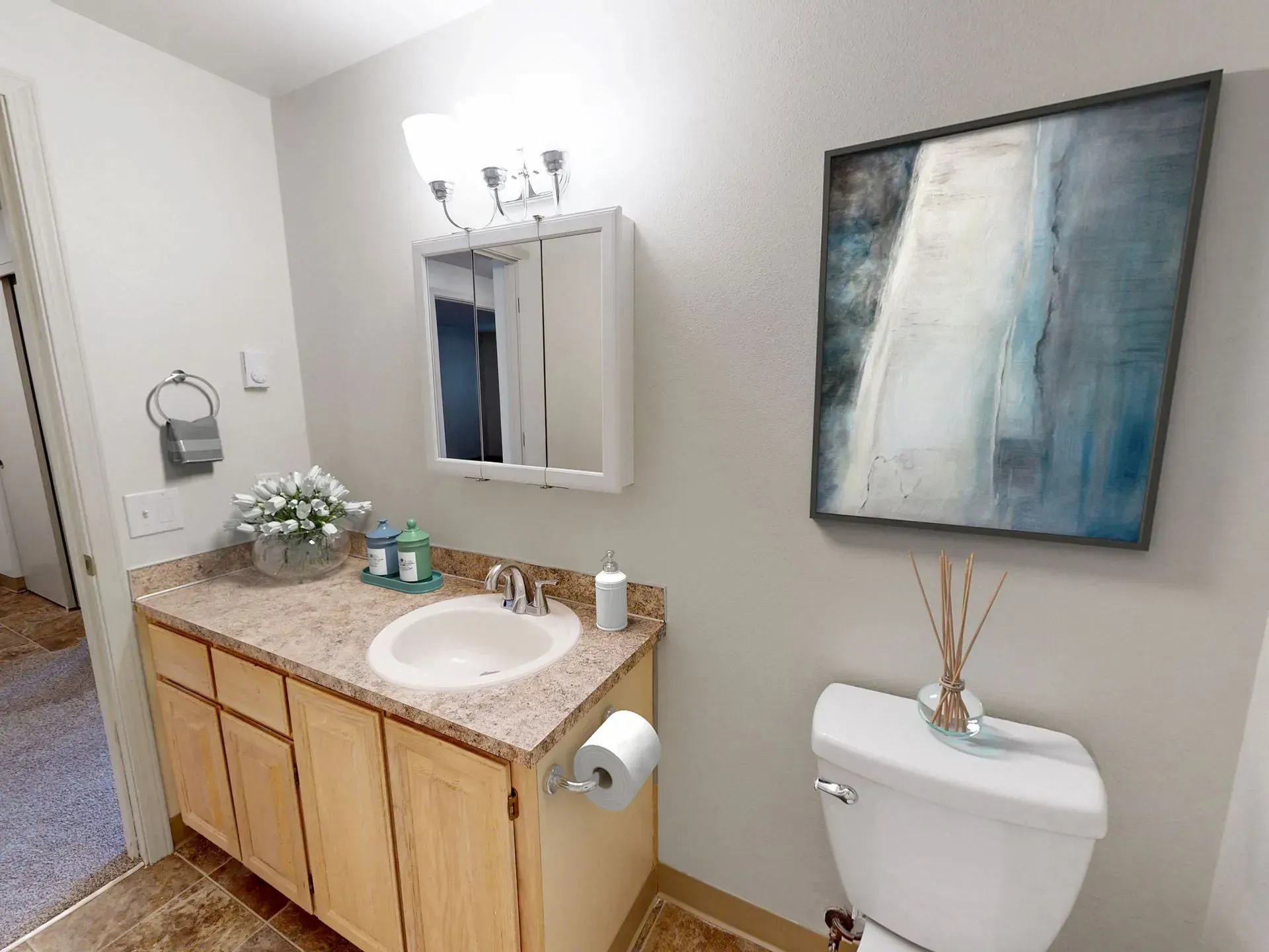 Bathroom with vanity, mirror, toilet, and artwork. Neutral color scheme.