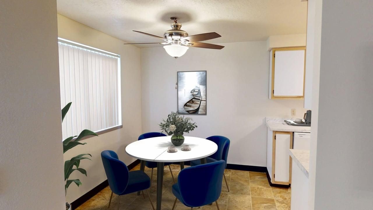 Dining room with round white table, blue chairs, a window with blinds, and cat art.