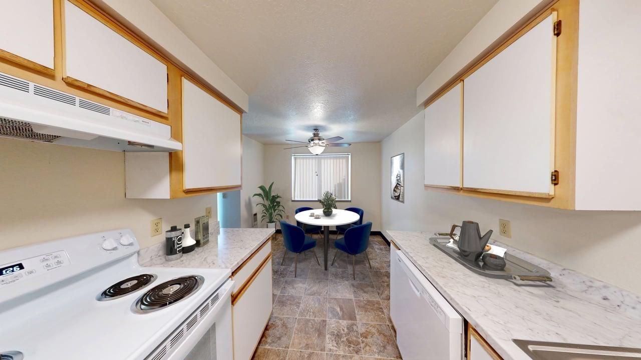 Kitchen with white cabinets, light countertops, and dining area with round table and blue chairs.
