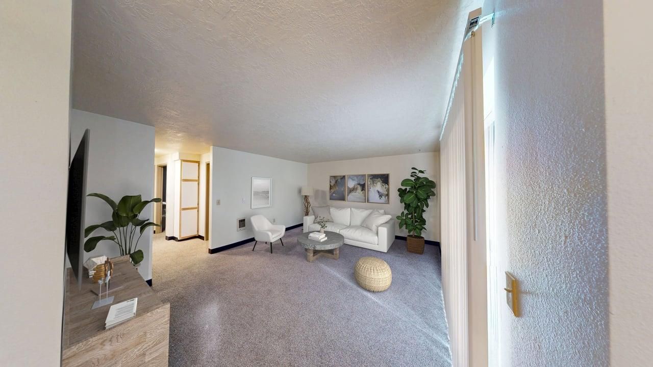 Spacious living room with carpet, sofa, and plants; doorway leads to hallway and a window on the right.