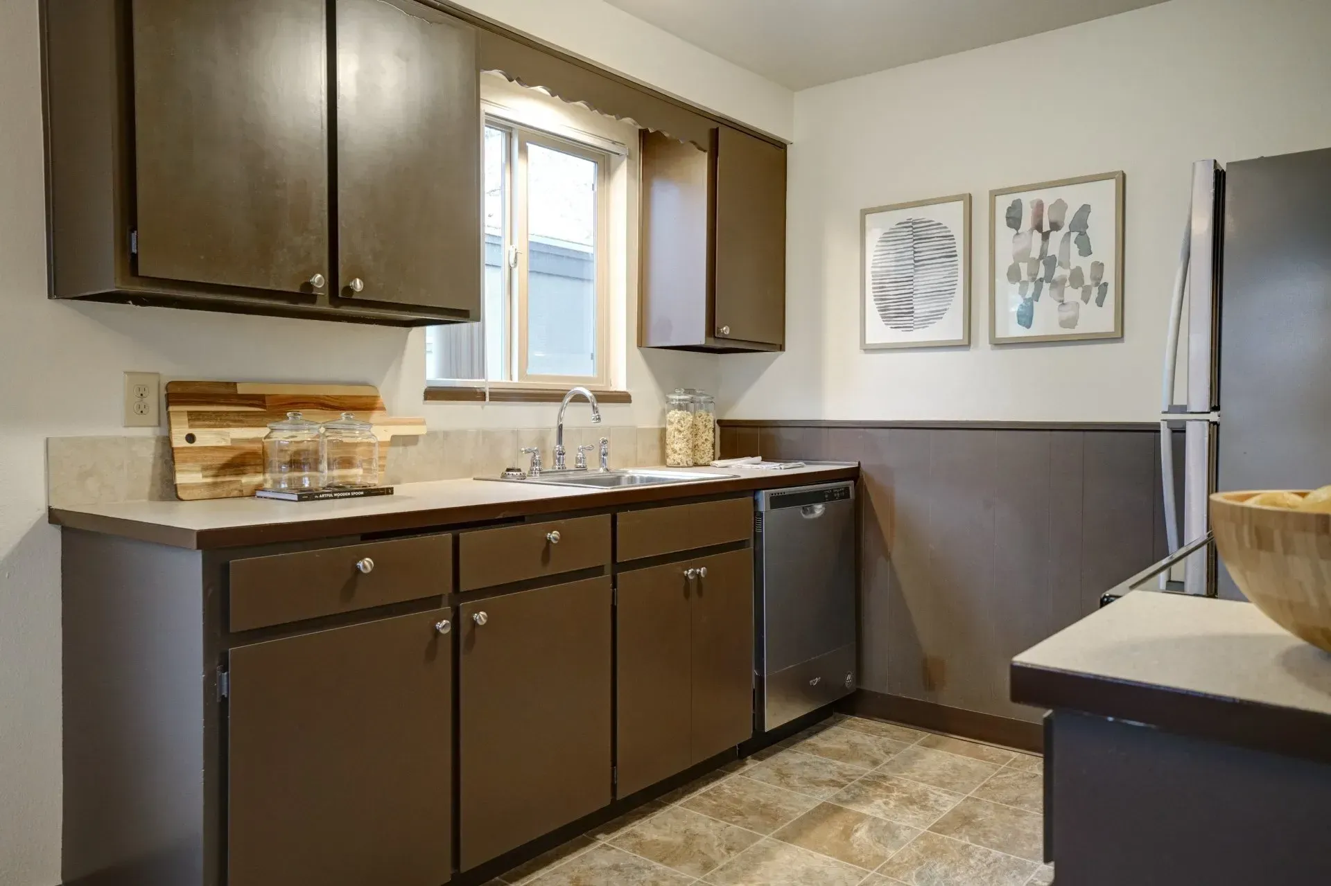 Brown-toned kitchen with cabinets, countertops, stainless steel appliances, and a window.