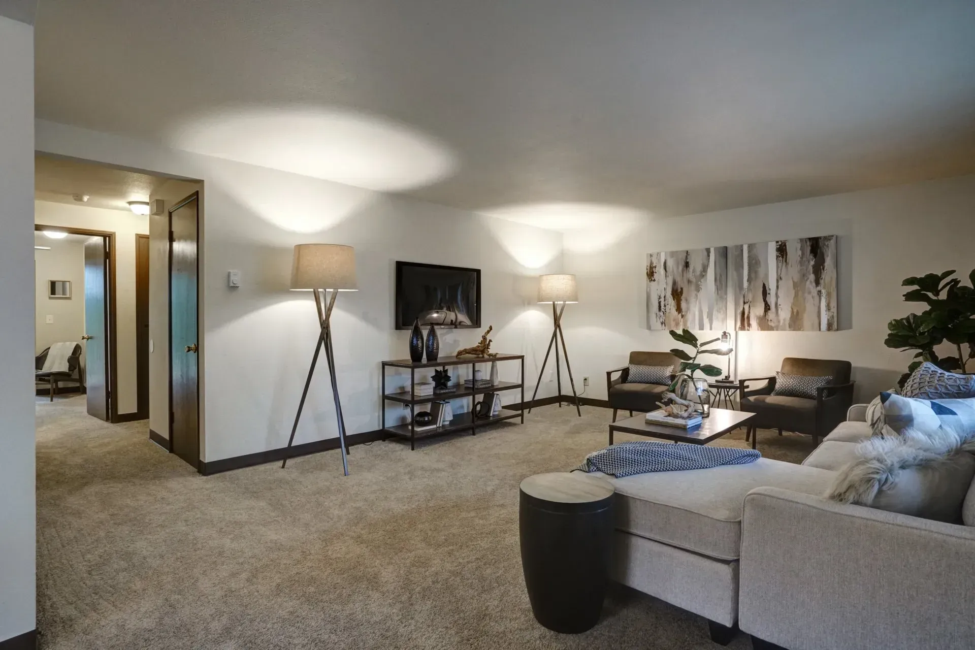 Living room with neutral tones, TV, seating, lamps, and a view into a hallway.