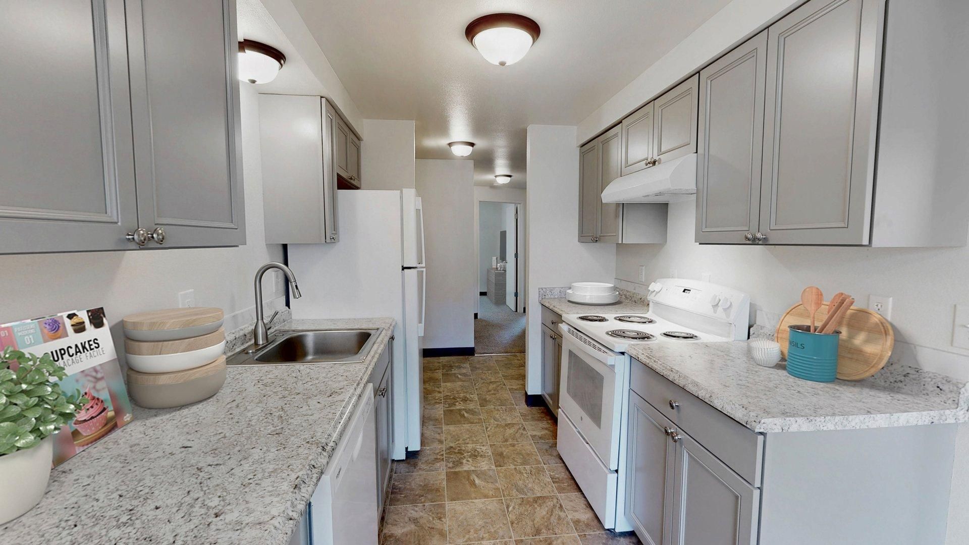 Kitchen with gray cabinets, white appliances, and speckled countertops.