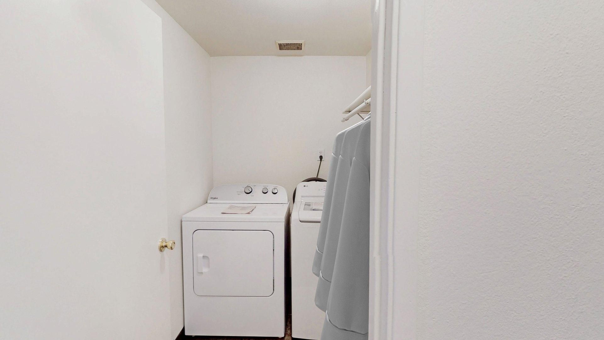 Laundry room with white appliances, clothing rack, and white walls.
