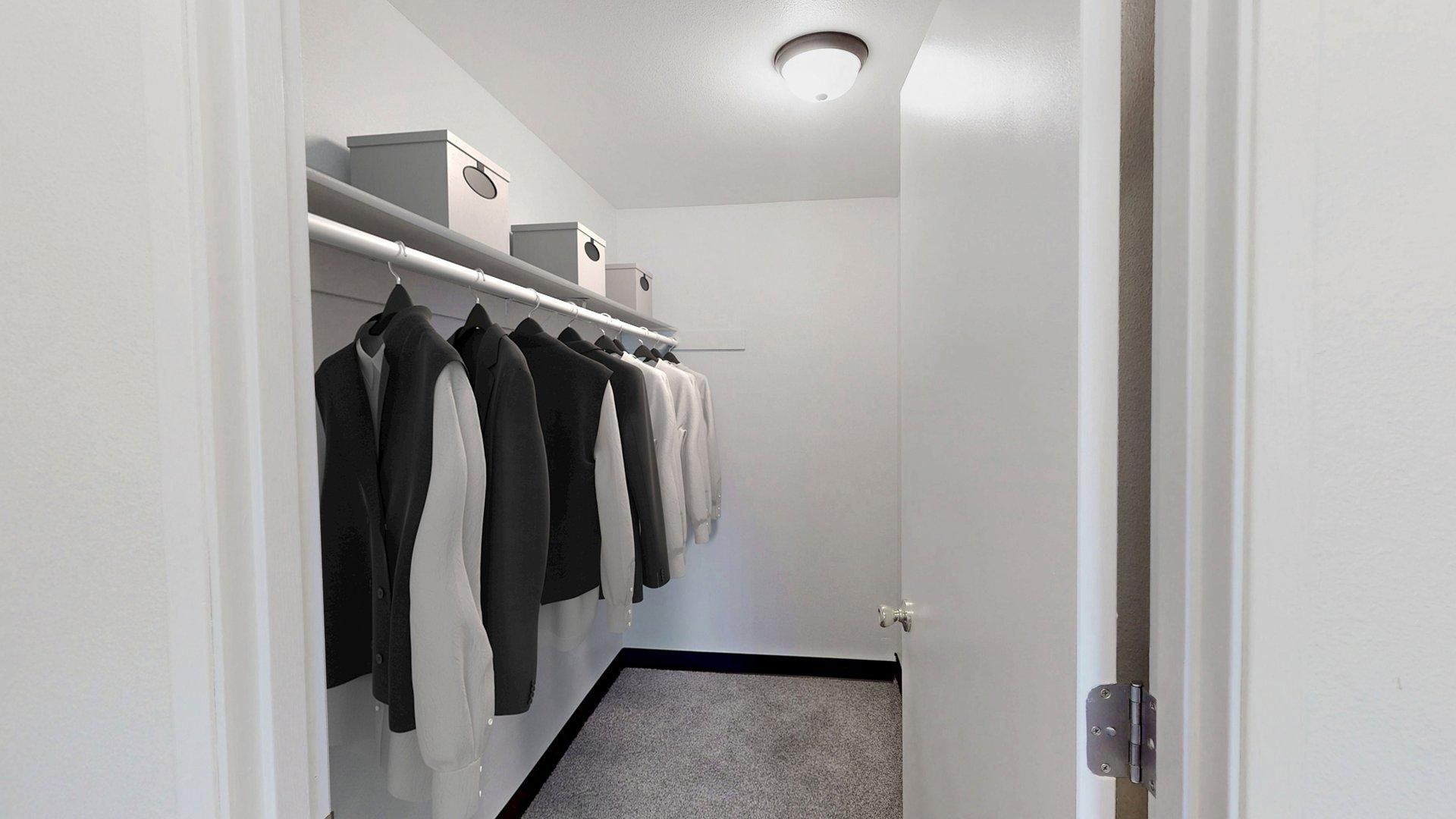 White closet with hanging clothes, storage boxes, and a light fixture.