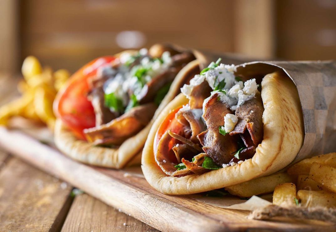 Two gyros and french fries on a wooden cutting board