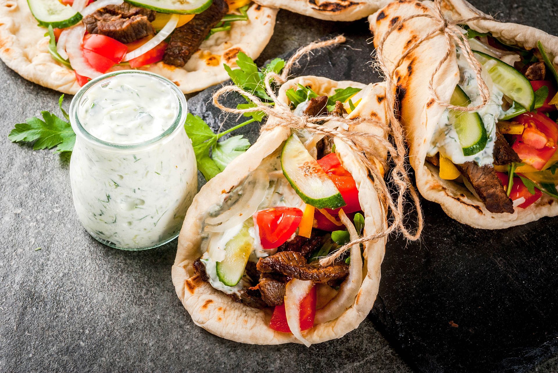 A close-up of a gyro with vegetables and a jar of yogurt on a table