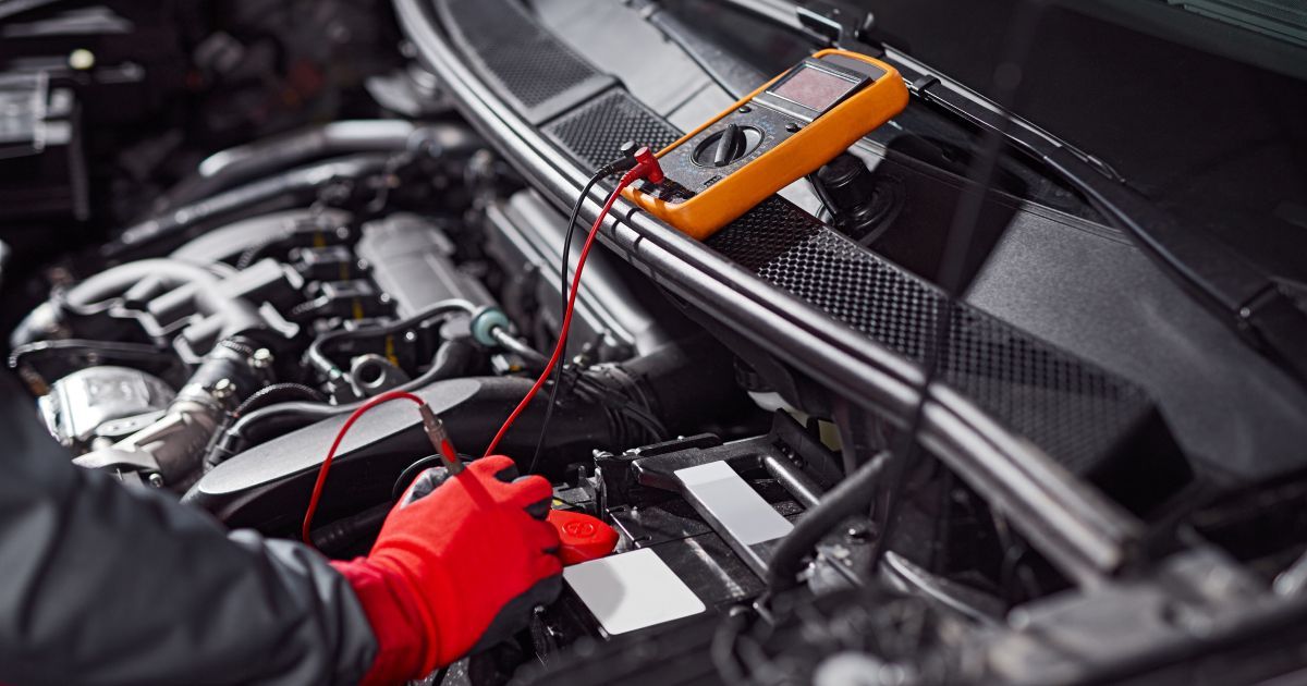 Mechanic using a red multimeter probe on a car engine in a repair shop