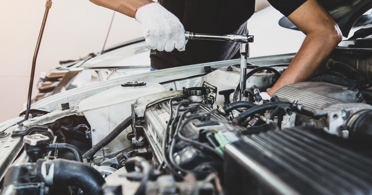 Mechanic working under a car hood with tools, inspecting the engine in a garage