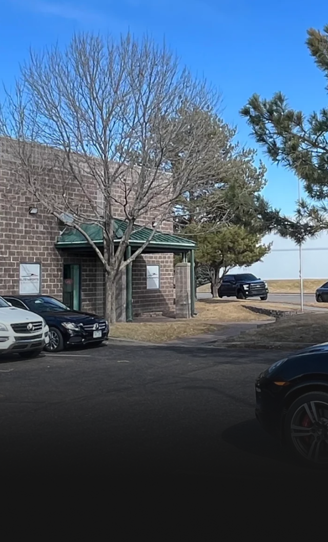 Parking lot by a building with parked cars, leafless trees, and a bright blue sky.