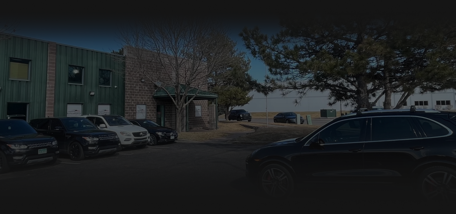 Parked cars beside a building and trees in a shaded lot