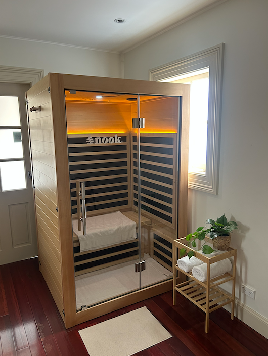 Wooden infrared sauna in a bright room, with warm interior lights and a small plant stand nearby  — Burwood Back Pain in Strathfield, NSW