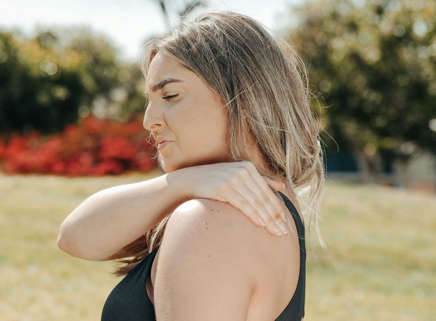 A Woman Is Holding Her Shoulder in Pain While Standing in A Field — Burwood Back Pain in Strathfield, NSW