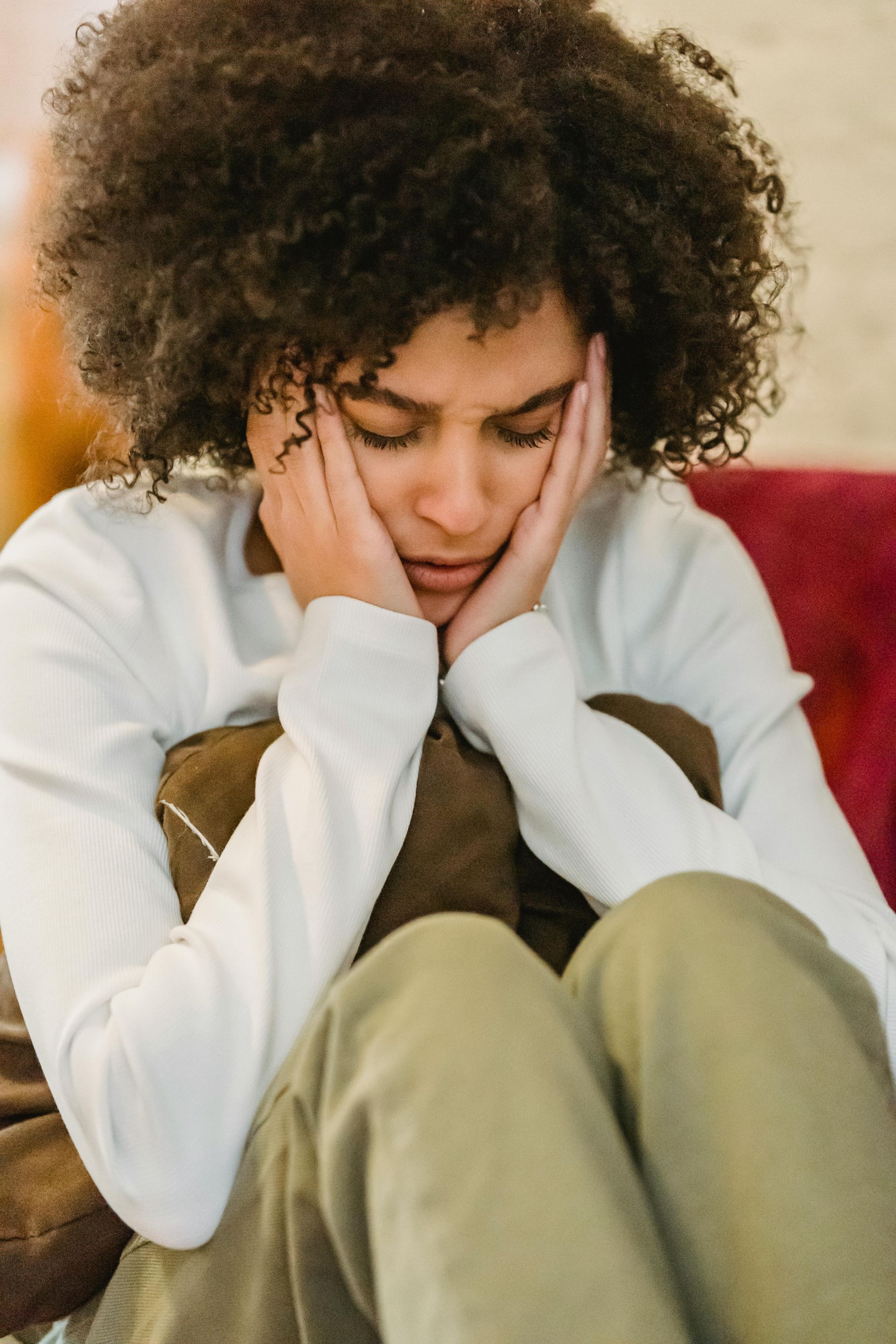 A Woman with Curly Hair Is Sitting on A Couch with Her Hands on Her Face — Burwood Back Pain in Strathfield, NSW