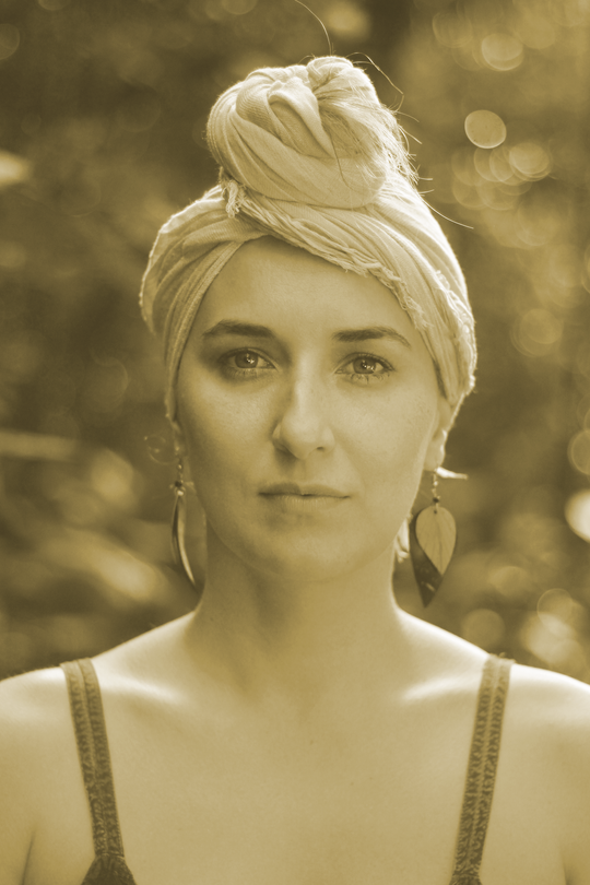 Retrato de uma mulher com um lenço na cabeça, olhando para a frente contra um fundo externo desfocado.