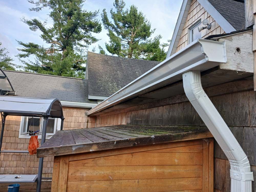 A white gutter is attached to the side of a house next to a wooden shed.
