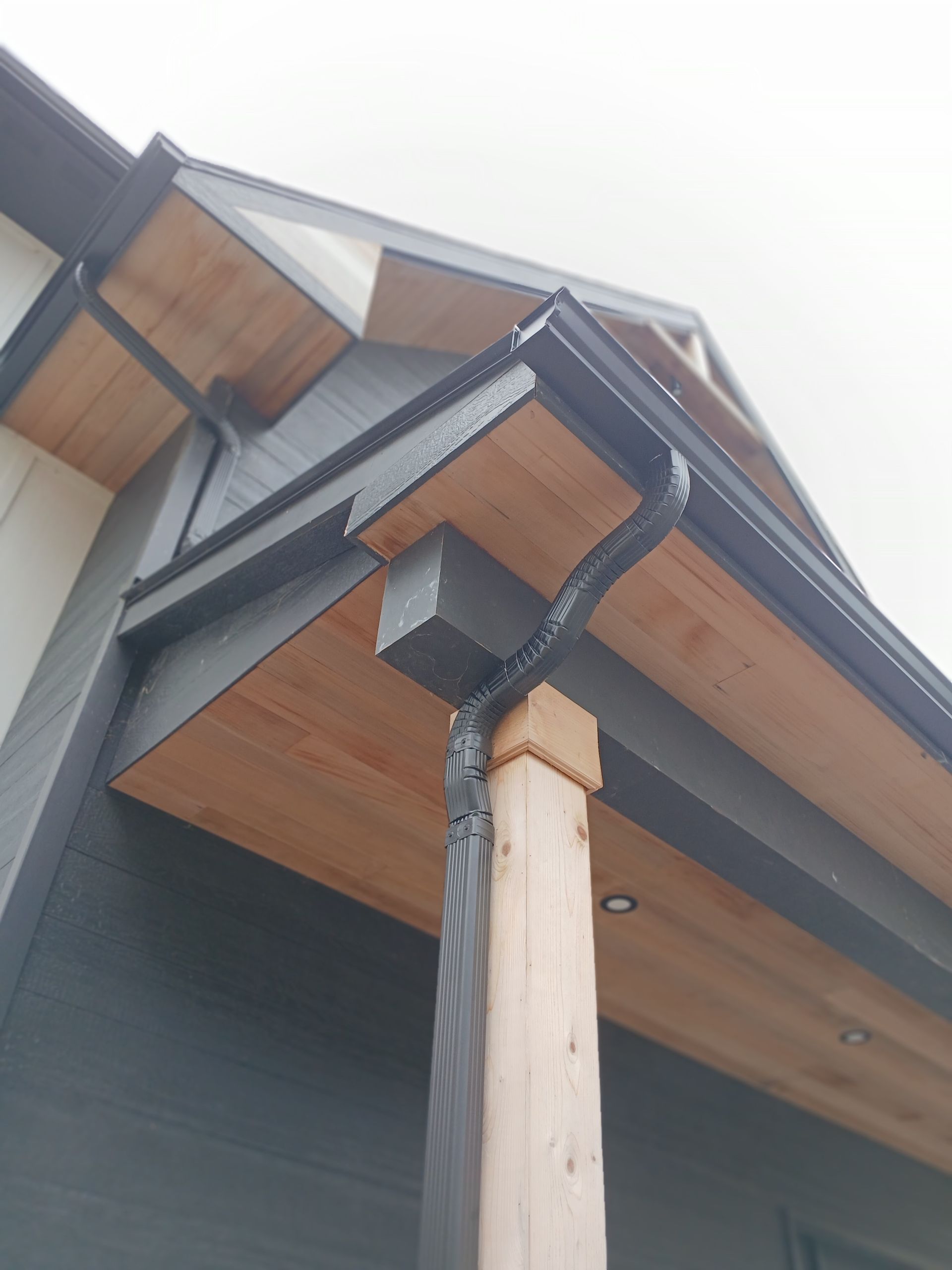 A white gutter is attached to the side of a house next to a wooden shed.