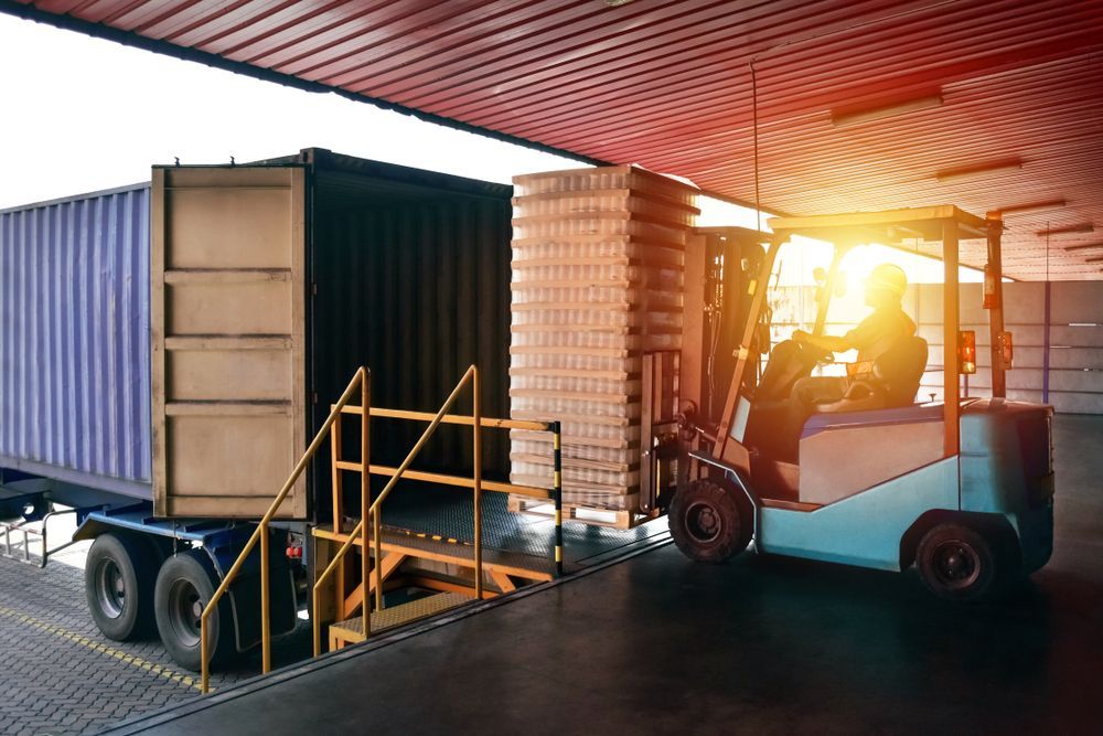 A Delivery Man Is Writing On A Clipboard In Front Of A Car Filled With Boxes — FNQ Freight & Logistics In Innisfail, QLD