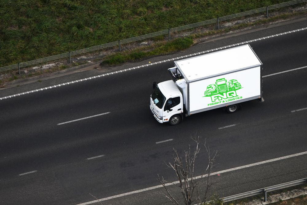 White delivery truck driving on a highway. Green foliage along the side— FNQ Freight & Logistics In Cairns, QLD