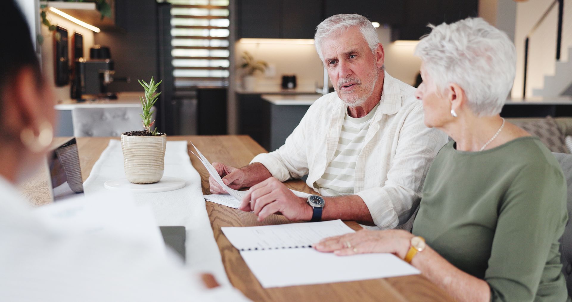 Two older adults reviewing documents with an advisor at a table in a modern home. Two older adults reviewing documents with an advisor at a table in a modern home.