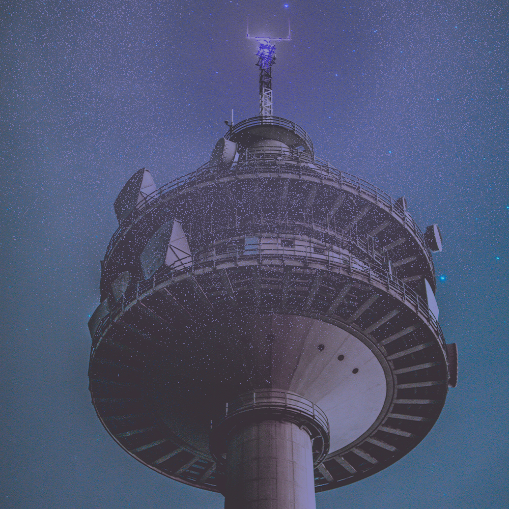 A tall communications tower at night under a starry sky.