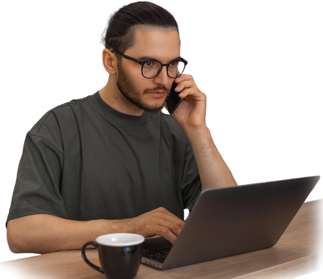 Man with glasses on a call, typing on a laptop, mug nearby.