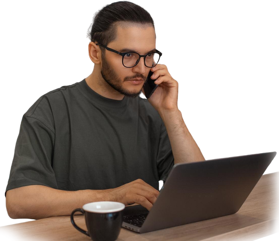 Man with glasses on a call, typing on a laptop, mug nearby.