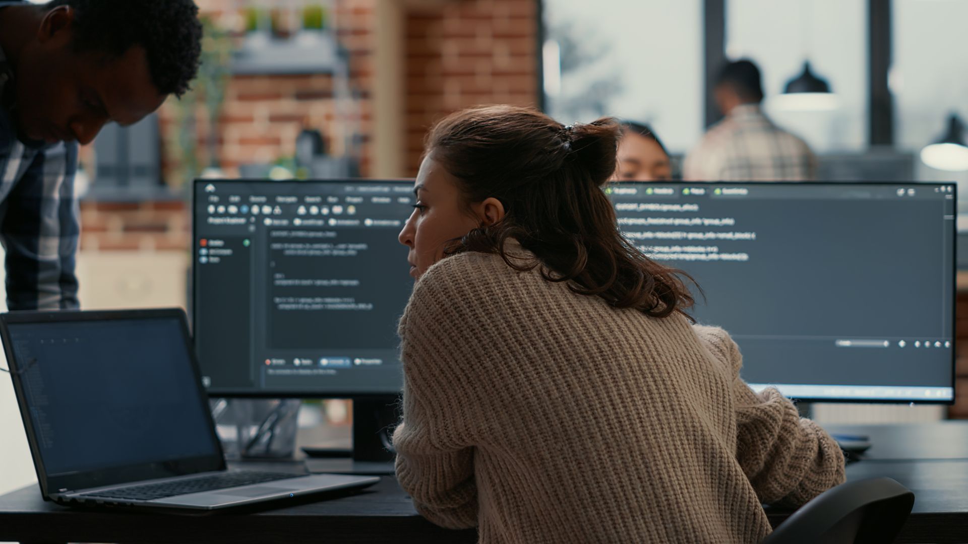 Woman at computer with code, two colleagues in an office.