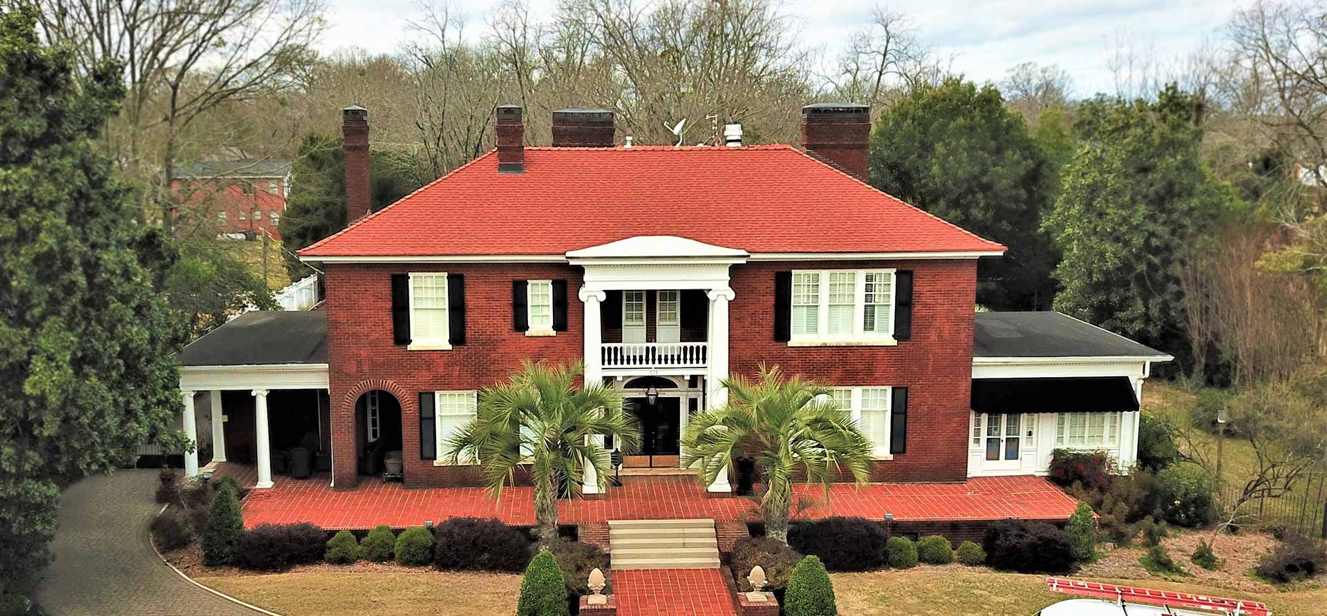 An aerial view of a large brick house with a red roof