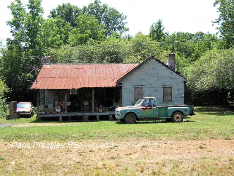 A truck is parked in front of an old house with a rusty roof